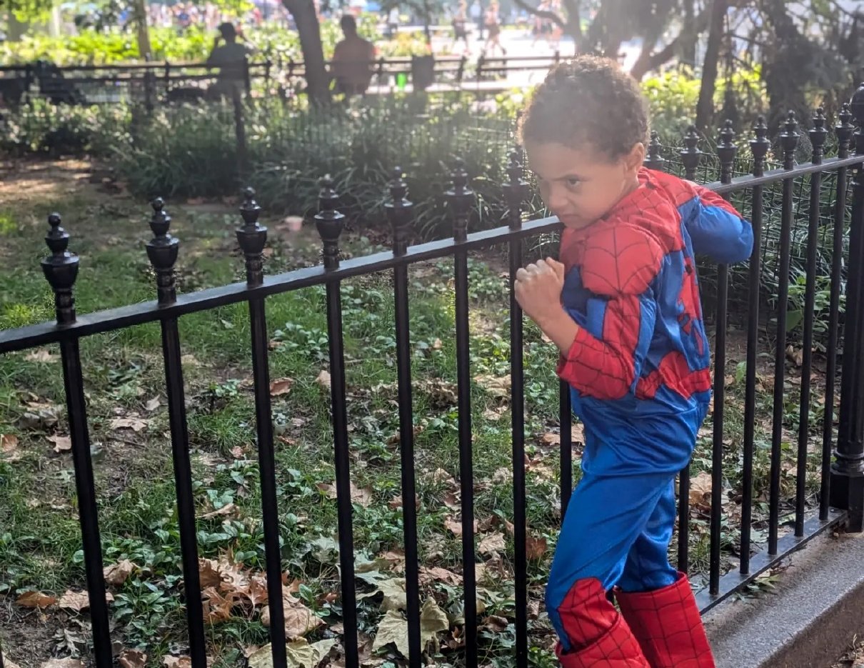 A young child in a superhero costume striking a brave pose in the park